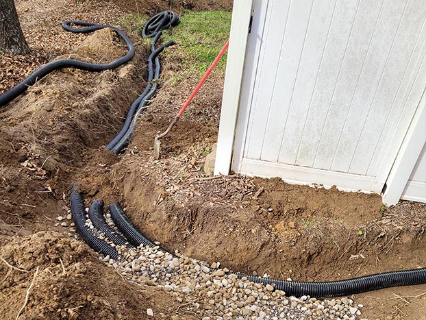 A freshly dug drainage ditch with black corrugated pipe laid out in preparation.