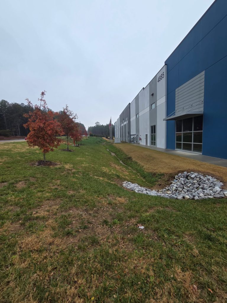 Commercial property with maintained turf, drainage swale, and young trees along the building exterior, showcasing professional groundskeeping in Chattanooga.