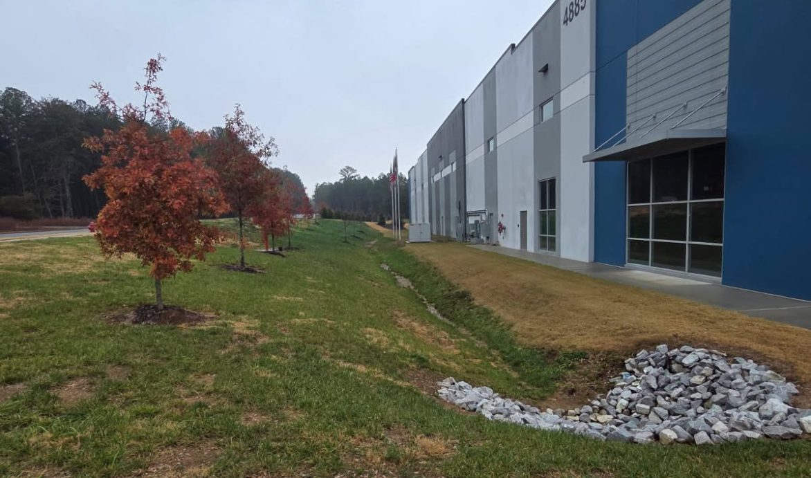 Commercial property with maintained turf, drainage swale, and young trees along the building exterior, showcasing professional groundskeeping in Chattanooga.