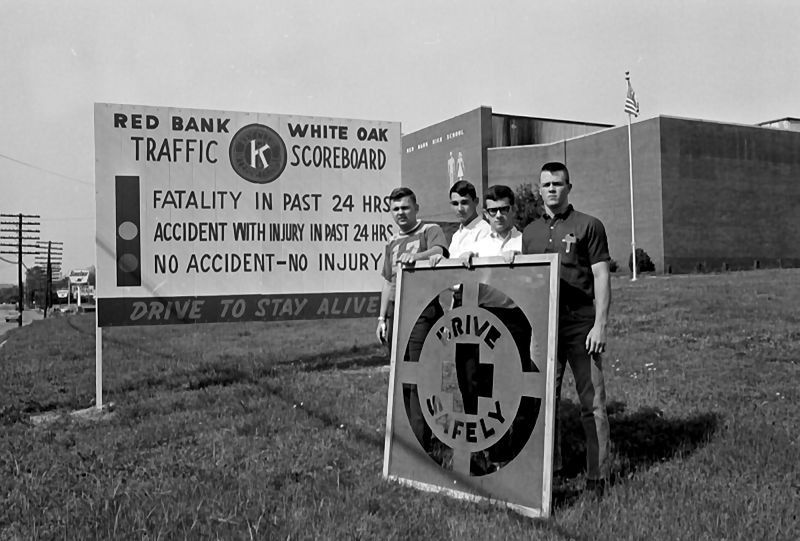 Four young men standing in front of the old Red Bank high school with a promotion sign that reads, "drive safely."